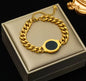 Gold chain bracelet with black circular centerpiece on a beige jewelry box