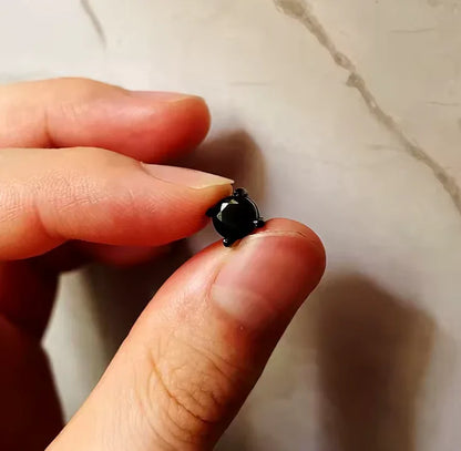 Hand holding a round black gemstone stud earring against a light marble background